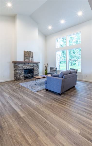 This is a spacious living room with a tall cathedral ceiling and large glass window on the side of the sofa set and coffee table across from the stone fireplace.