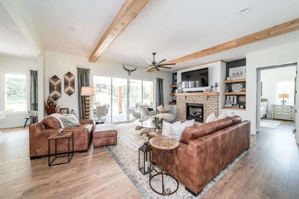 Living room with brown leather seats, a beamed ceiling, and a brick fireplace topped with a wall-mounted TV.