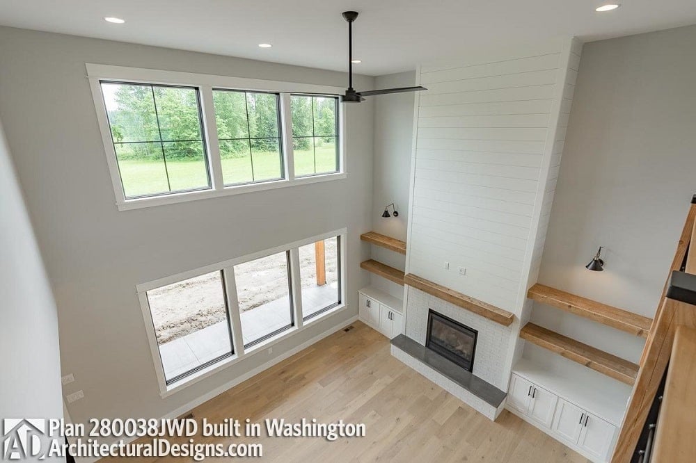 This is a view of the living room from the vantage of the indoor balcony. The living room has a tall ceiling, large transom windows and a large fireplace in the middle of built-in shelves and cabinets.