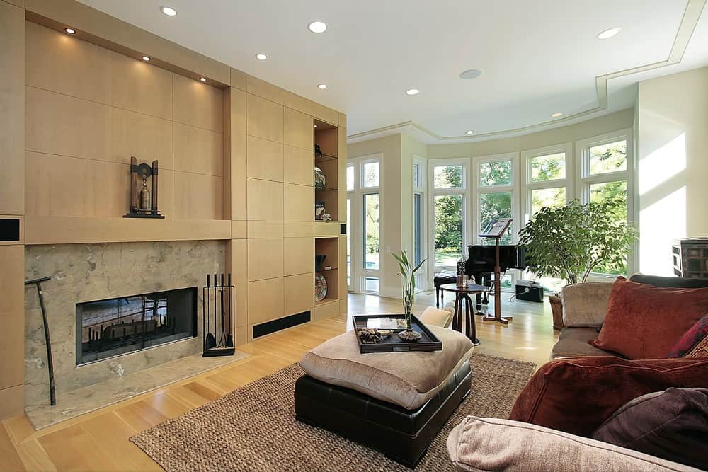This formal living space features hardwood flooring and a brown fireplace with built-in shelving on the side. The large brown comfy couch is set in front of the fireplace.