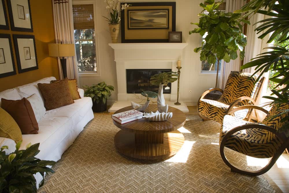 Large formal living room featuring a white couch and a round center table set on a stylish brown rug. The room is surrounded by brown walls. It also has a fireplace.