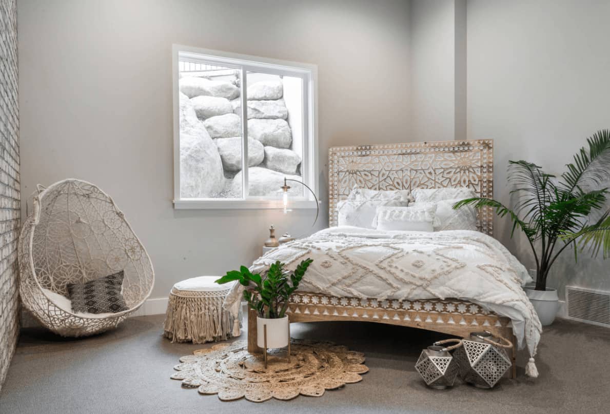 Stylish bedroom offers a stunning bed and knitted chair placed against the brick accent wall. It includes green potted plants and a picture window framing the large white rocks.