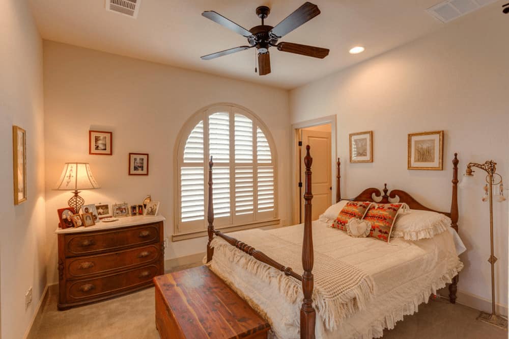 Ambient light from the table lamp and recessed ceiling lights create a warm and cozy feel in this Mediterranean bedroom with a four poster bed and a storage bench that complements the wooden drawer chest.