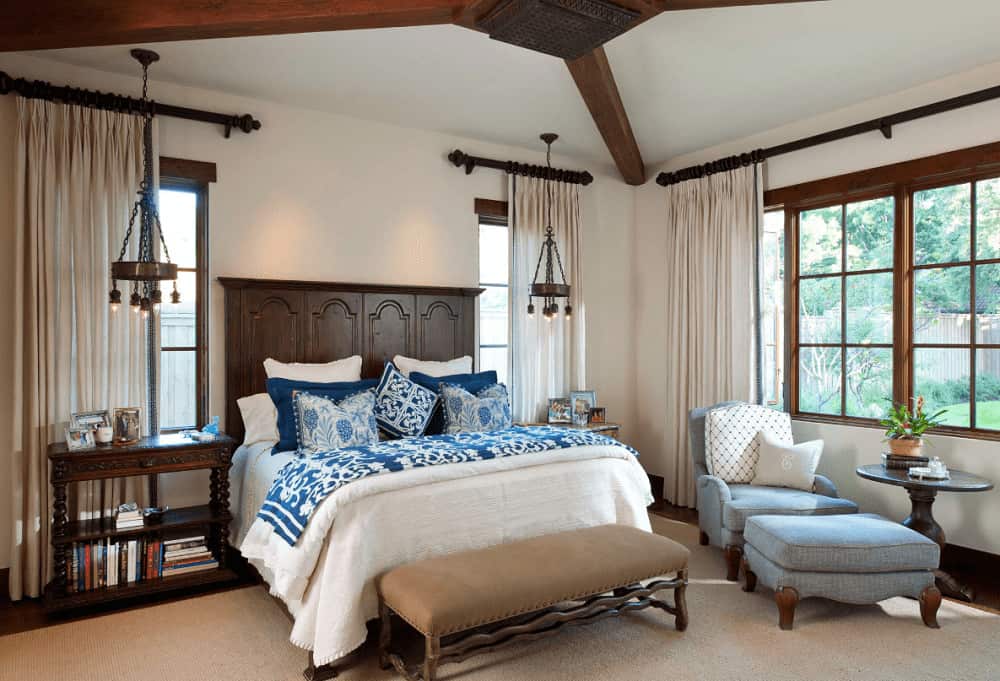 A pair of vintage pendant lights illuminate the nightstands in this Mediterranean bedroom with a wooden bed and blue lounge chair that sits next to the round side table.