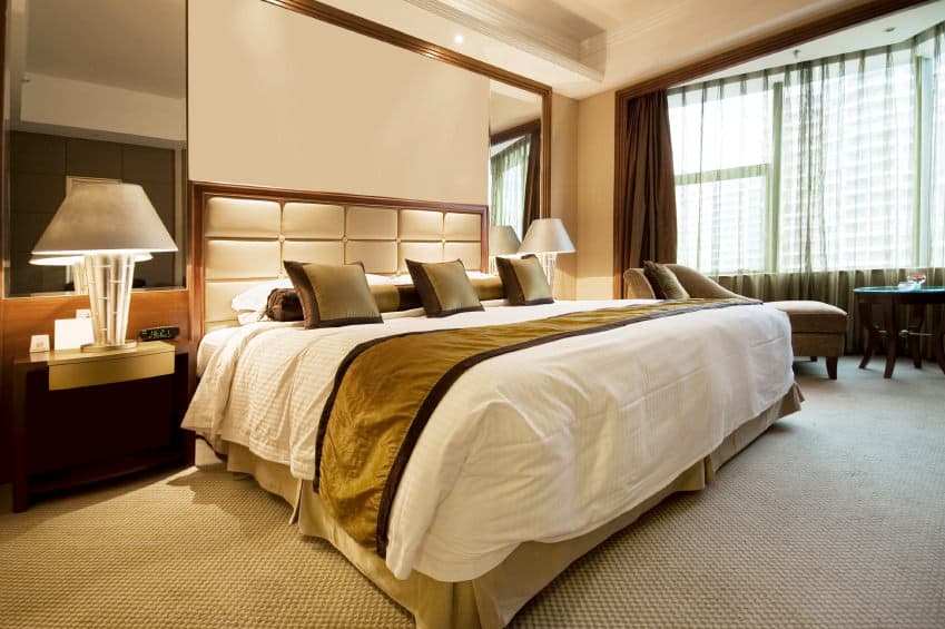 Primary bedroom boasting a gorgeous bed setup lighted by table lamps on both sides. The tray ceiling looks absolutely charming. The room also has carpeted flooring.