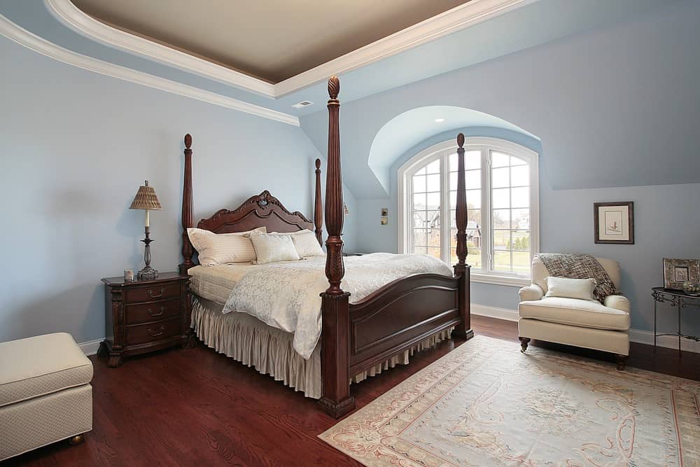 A primary bedroom featuring blue walls and reddish hardwood flooring topped by a classy area rug.