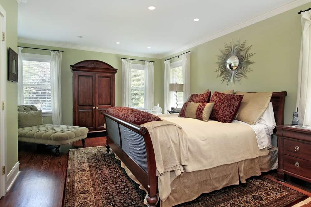 A focused look at this primary bedroom's large cozy bed set on top of the area rug covering the hardwood flooring. The room is surrounded by green walls.