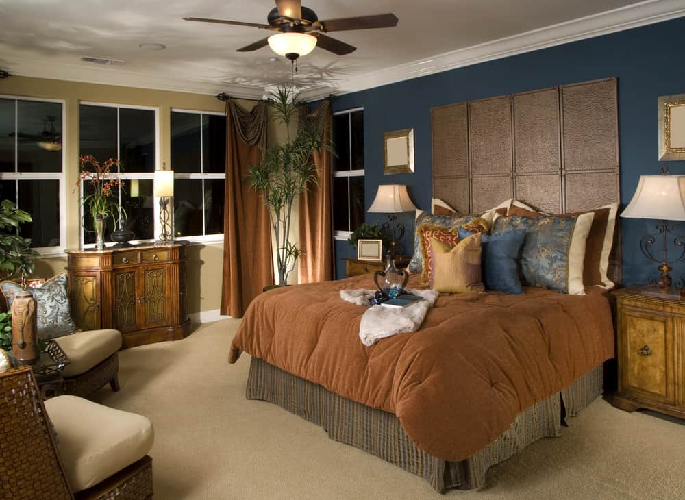 A primary bedroom with blue and beige walls along with fine carpet flooring. The room also offers a super comfy bed lighted by two table lamps on both sides.