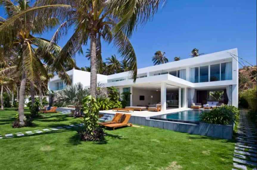 The modern elements of this home works well with the Tropical-style landscaping that gives a counterbalance to its sharp angles and stark brightness. The front yard of this home is filled with a healthy carpet of grass with embedded stone steps for the walkway shaded by tall palm trees.