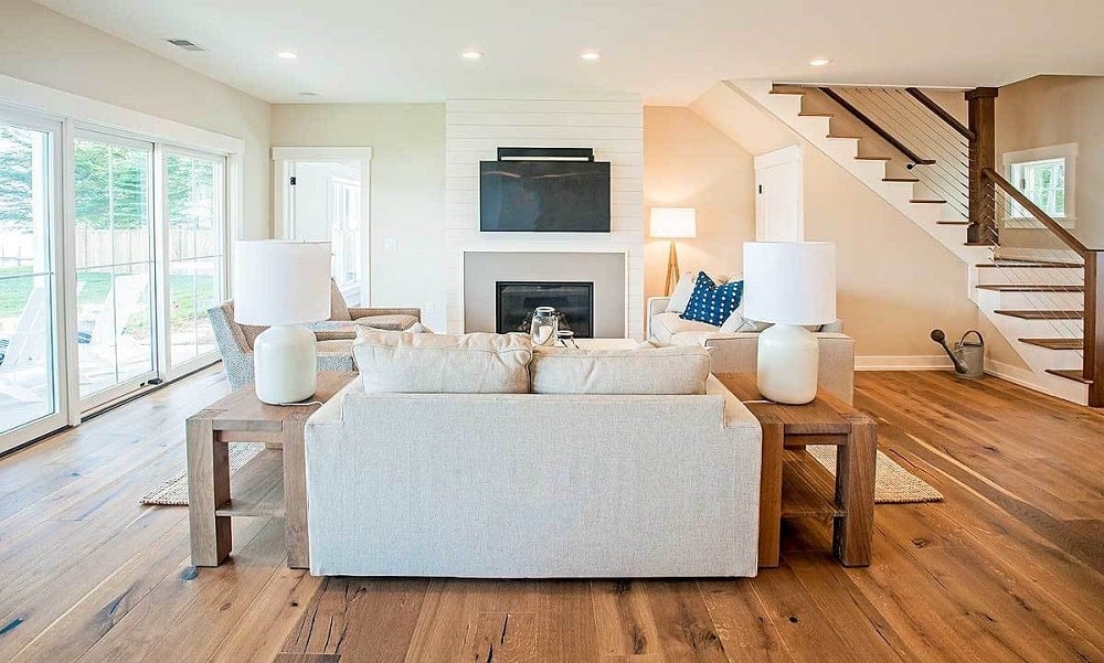 This is a simple and comfortable living room with a beige sofa set across from a fireplace embedded into a shiplap white wall that also houses the wall-mounted TV.