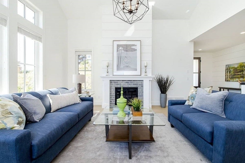 This living room has a pair of blue sofas flanking the glass-top coffee table across from the fireplace that is topped with a wall art.