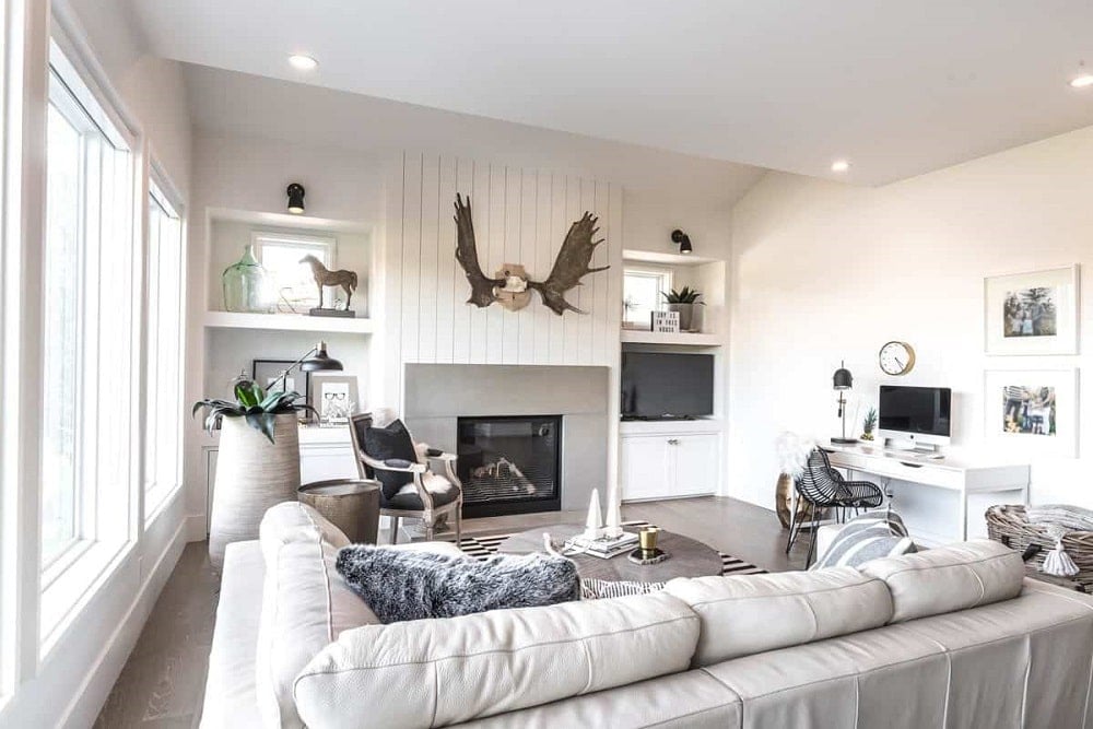 The living room features a light gray sectional and a modern fireplace fitted on the beadboard pillar.