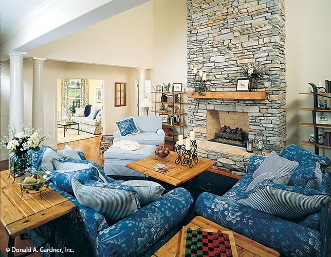 This is a close look at the living room that has a stone mosaic fireplace across from the floral cushioned chairs that match the blue tone of the area rug contrasted by the wooden tables.
