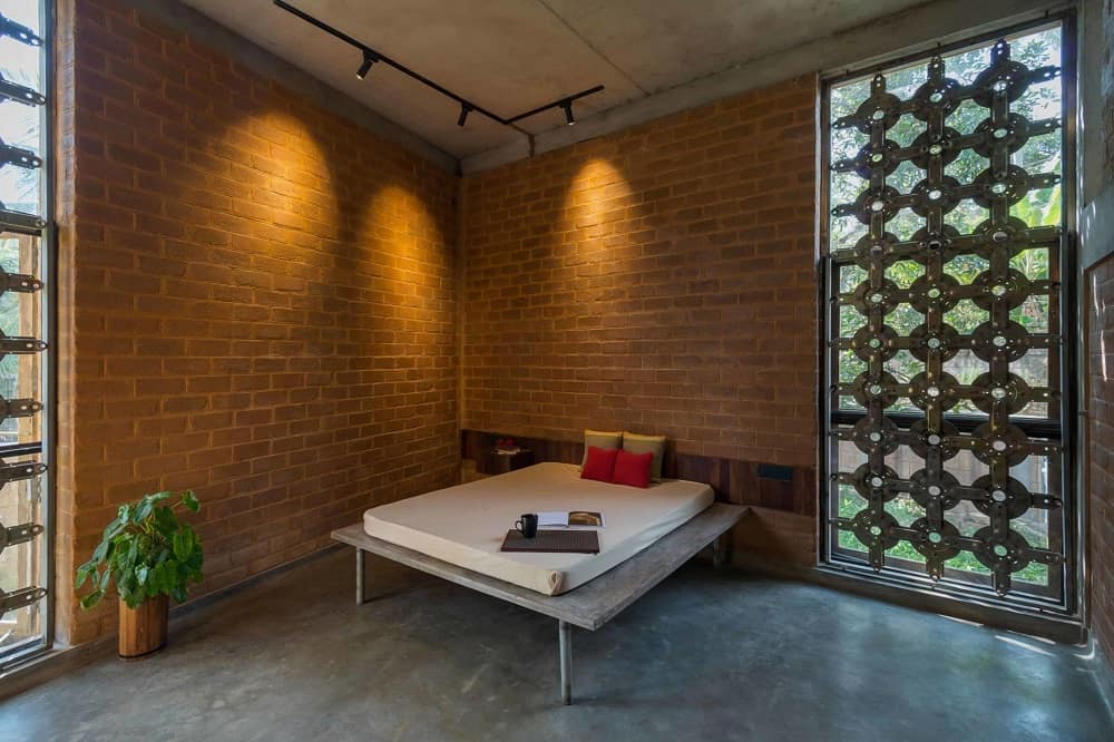 This is a close look at the spacious bedroom with a platform bed placed at the far corner of the red brick walls. These are then complemented and brightened by the patterned panels of the glass walls that filter light in.