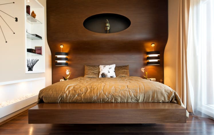 A focused shot at this primary bedroom's modern bed set with stylish wall lights. There are built-in shelves on the white wall beside the bed set.