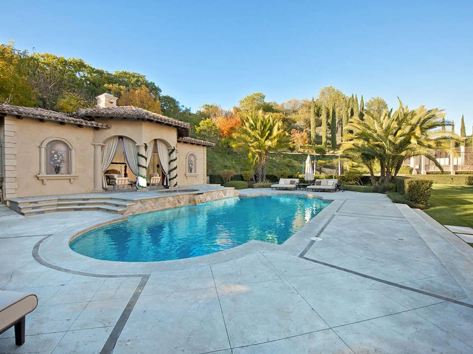 A large outdoor area featuring a garden and lawn space along with a Mediterranean-style swimming pool with sitting lounges.