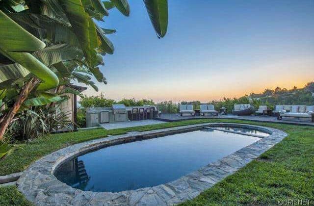 A large outdoor area boasting a lawn area surrounding the oval-shaped swimming pool with sitting lounges and an outdoor sofa set on the side.