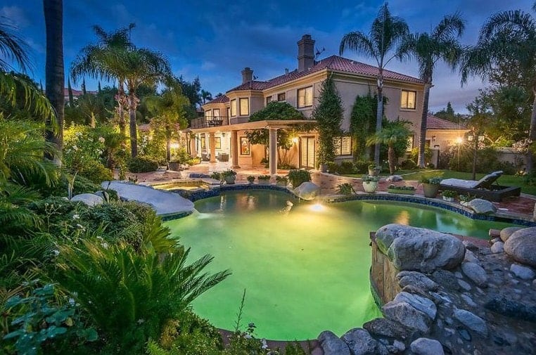 A mansion boasting a lavish garden with healthy plants and trees, along with a custom-made swimming pool.