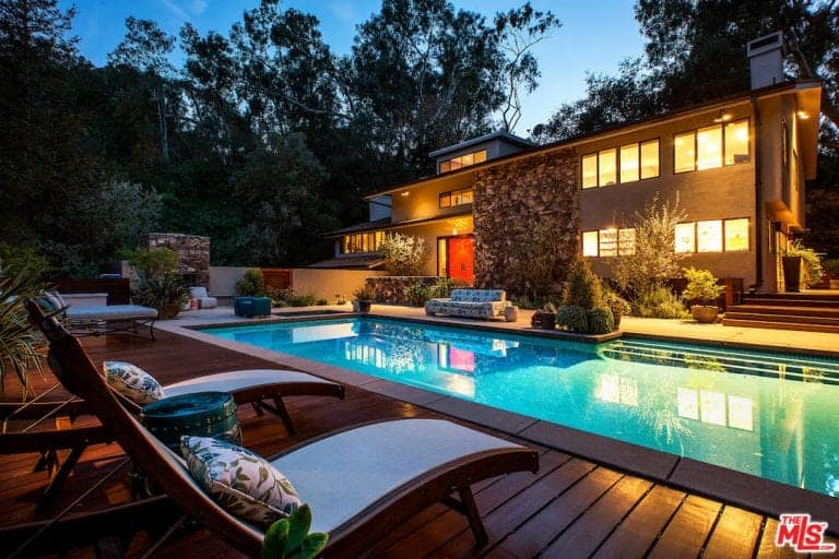 A modern house with a modern outdoor area. It offers a spacious deck area and a rectangular swimming pool.