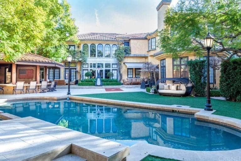 A mansion with a gorgeous outdoor area featuring an outdoor bar, a nice set of sitting areas and a Mediterranean-style swimming pool.