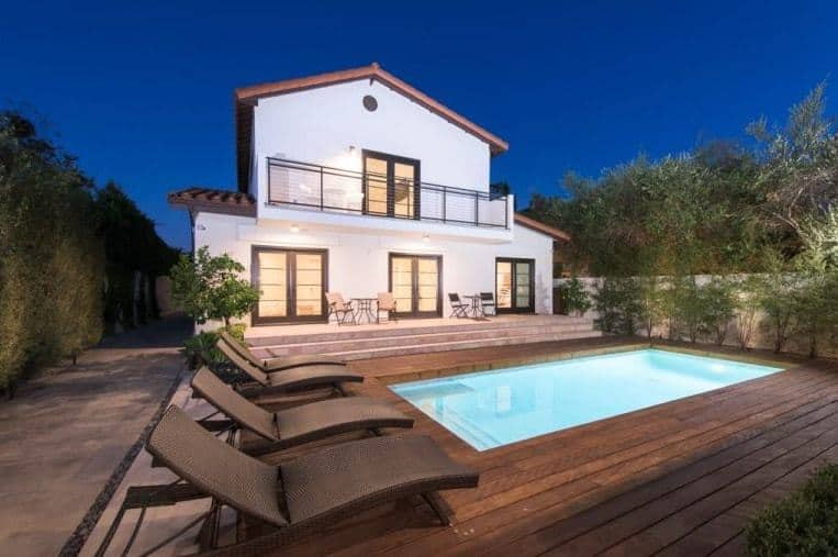 A look at this house from its backyard featuring a deck with sitting lounges, surrounding the rectangular swimming pool.
