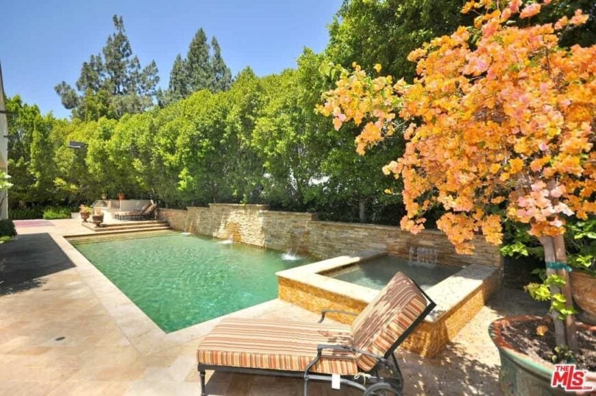 This outdoor area offers a rectangular swimming pool surrounded by mature and healthy trees. There's a sitting area on the side as well.