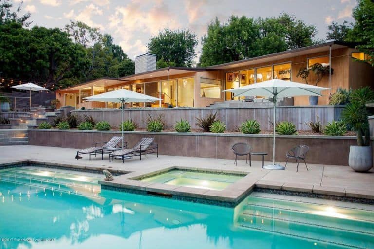 A large outdoor area boasting a patio and multiple sitting lounges, along with a large rectangular swimming pool.