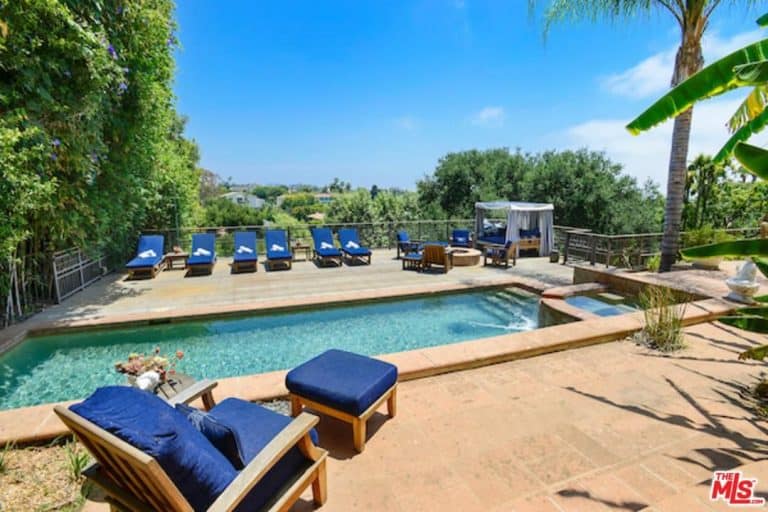 A nicely set outdoor area with multiple lounges and a rectangular swimming pool surrounded by tall and mature trees.