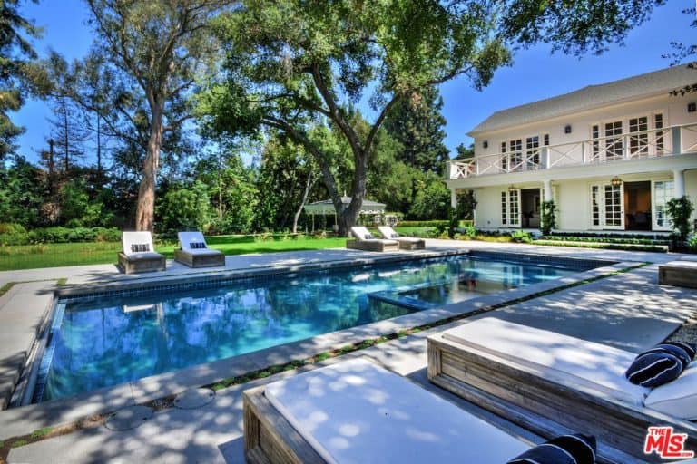 A spacious backyard with beautiful lawn area and a large rectangular swimming pool with lounging seats on both sides.