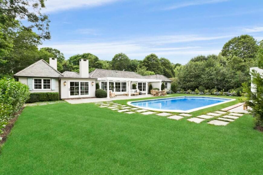 A spacious backyard featuring a well-maintained lawn area with stylish walkway, along with a large swimming pool area.