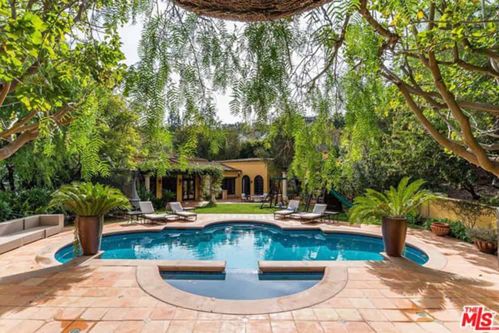 A beautiful Mediterranean-style swimming pool with sitting lounges on the side and is surrounded by healthy plants and trees.