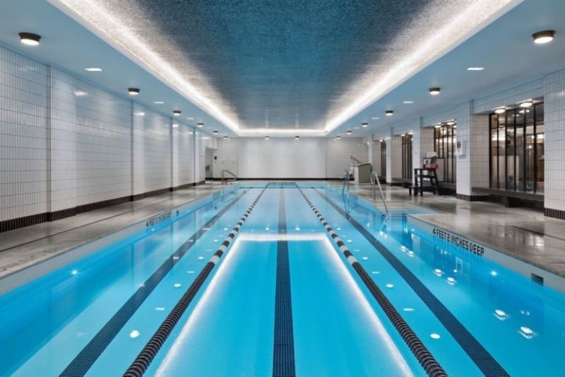 A large indoor swimming pool area with a tray ceiling and recessed ceiling lights.