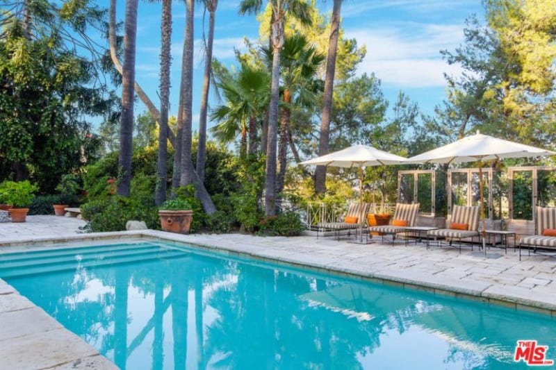 A close up look at this home's swimming pool situated outside surrounded by the beautiful green plants and trees.