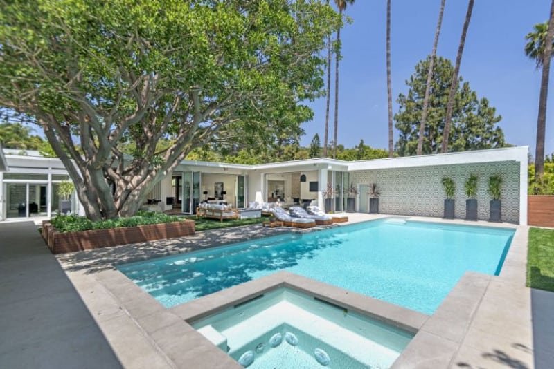 An outdoor area featuring a custom-made swimming pool with a large tree giving shade to the place.