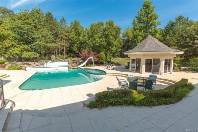 A beautiful outdoor area featuring a modern cottage and a custom-made swimming pool. The property is surrounded by tall and mature trees.