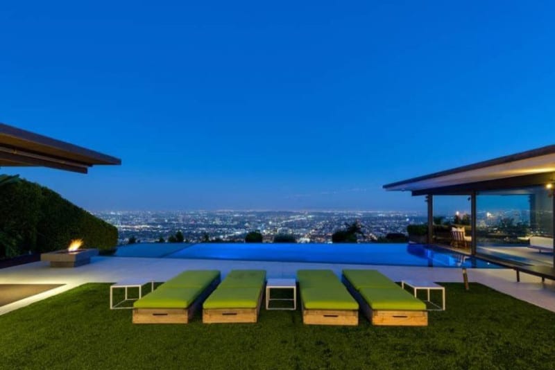 A modern house with a modern outdoor area featuring a well-maintained lawn and stylish sitting lounges along with an infinity pool on the side.
