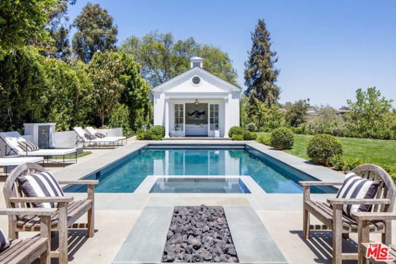 A focused look at this home's backyard featuring a rectangular swimming pool with multiple sitting lounges and a sitting area with a firepit, along with a lawn area on the side.