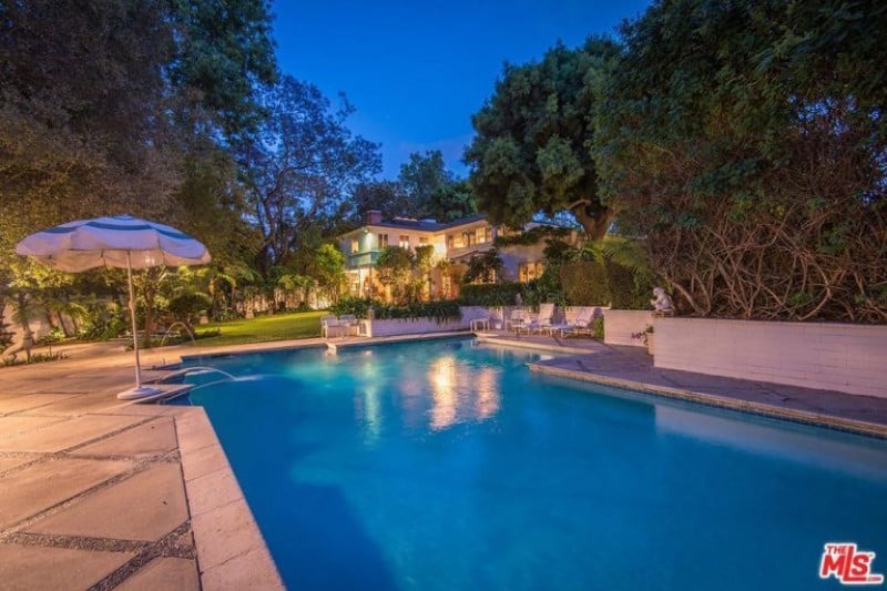 A large outdoor area featuring a custom swimming pool surrounded by large and mature trees. The outdoor area also has a beautiful garden.