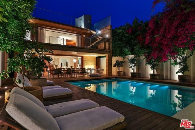 A modern home with an outdoor area featuring a deck surrounding the rectangle swimming pool. There's also an outdoor dining table set on the side.