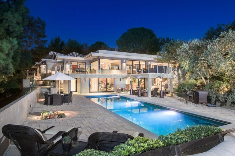 Large modern house featuring a swimming pool and multiple sitting lounges, along with an outdoor dining table set.