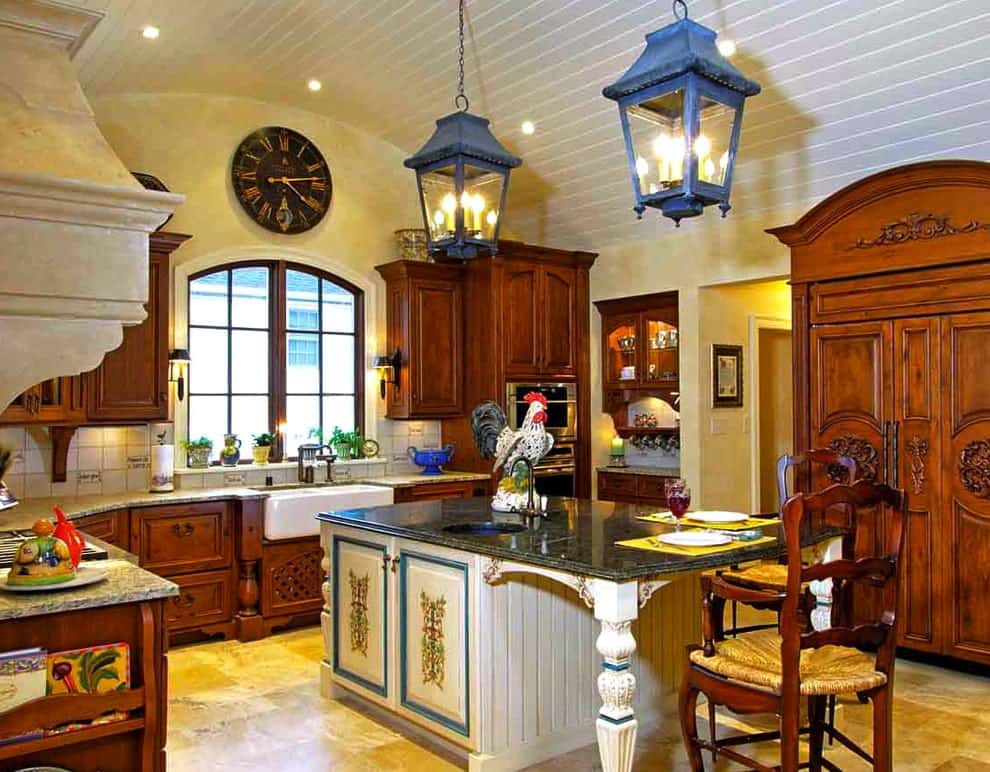 Wooden cabinets surround a beadboard breakfast island that's topped with a black granite counter and a round sink. It is illuminated by lantern pendant lights that hung from the barrel vaulted ceiling.