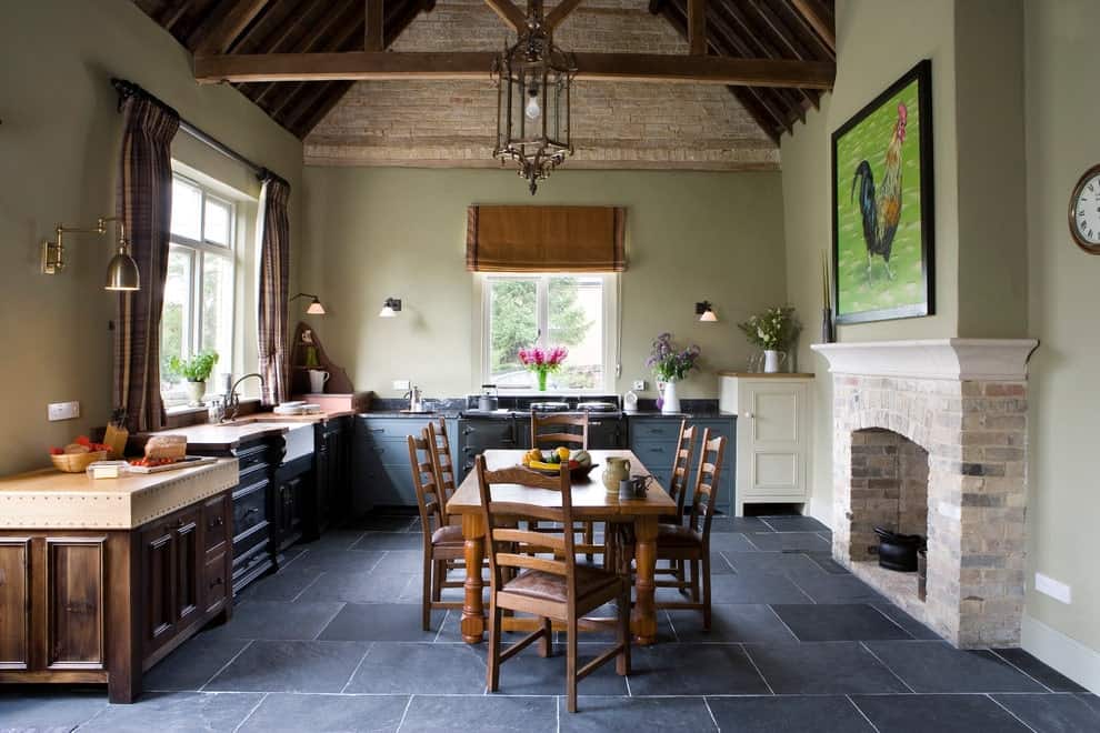 This kitchen is decorated with a chicken wall art and a gorgeous chandelier that hung over the wooden dining set. It has multi-colored cabinets and a brick fireplace fixed against the beige wall.