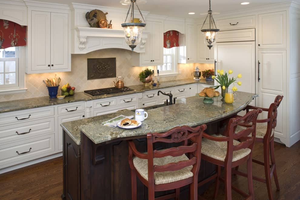 Red printed valances stand out against the framed windows and white cabinetry in this kitchen with glass pendant lights and a two-tier breakfast island paired with redwood counter chairs.