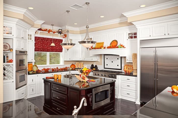 A red dotted roman shade covering the picture window stands out against the white cabinetry in this kitchen with stainless steel appliances and a dark wood island lighted by glass dome pendants.