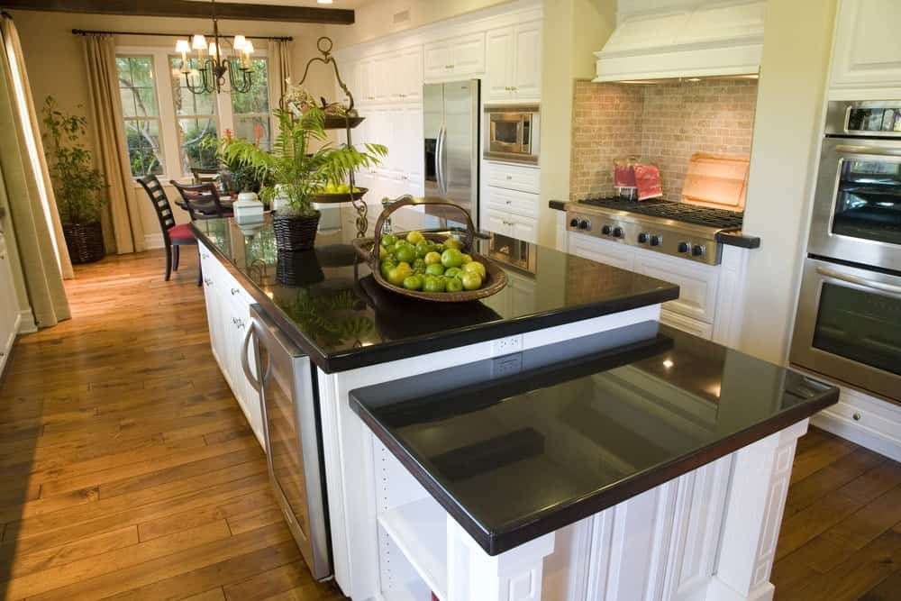 Absolute black granite countertops create a striking contrast to the white cabinetry and kitchen island that's fitted with built-in storage and wine fridge. There's round dining set by the framed windows lighted by a wrought iron chandelier.
