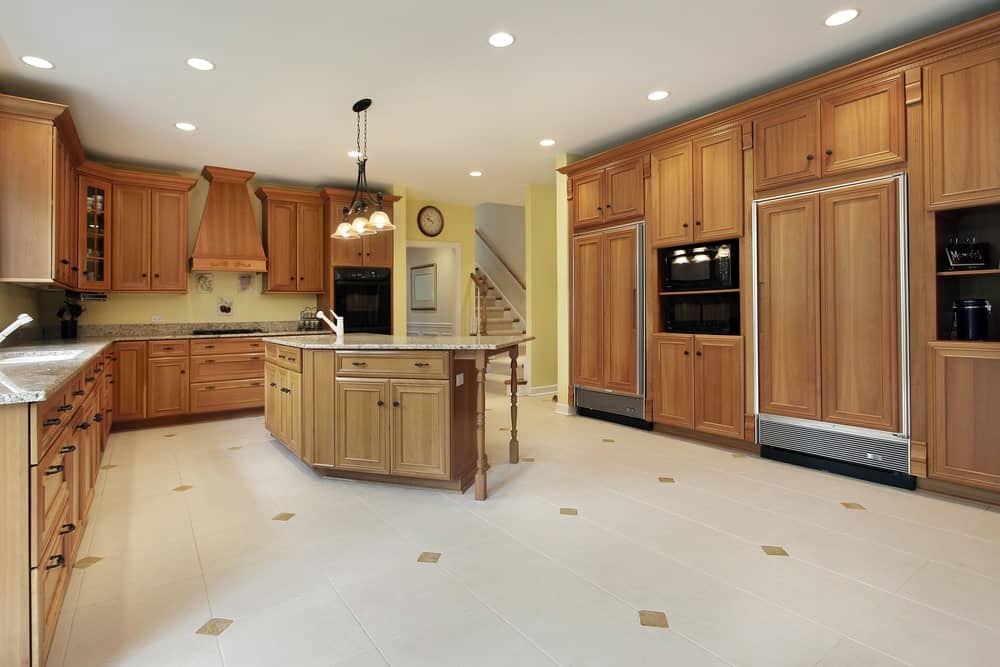 Spacious kitchen with black appliances and wooden cabinetry matching with breakfast island for a unified look. It is illuminated by glass dome pendants and recessed ceiling lights.