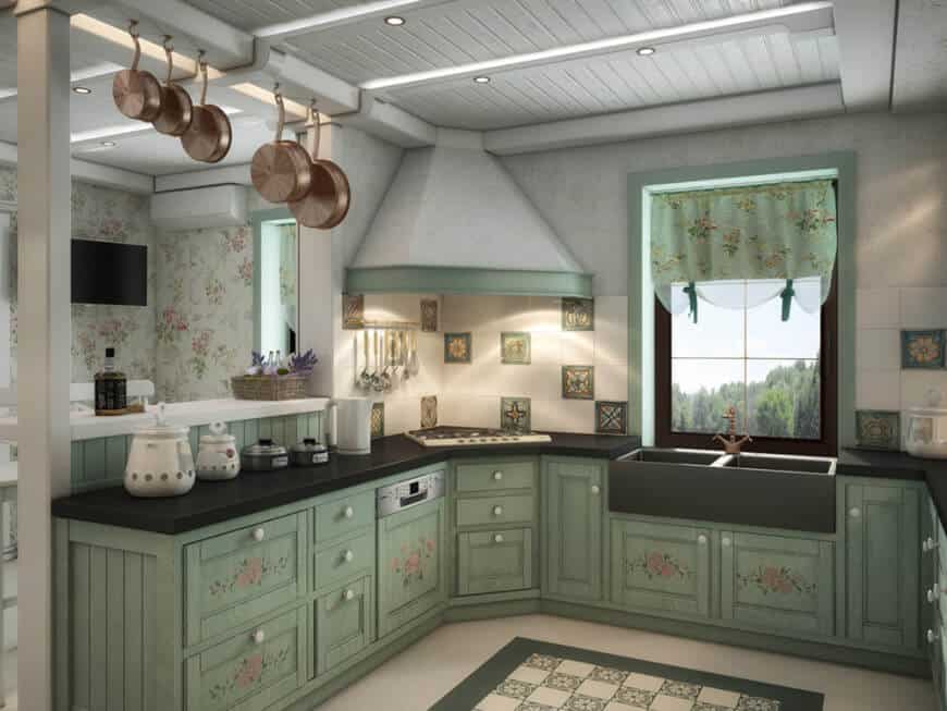 Charming kitchen with copper pots and green cabinets topped with dual sink and absolute black granite counters. It includes a gray range hood and a glazed window dressed in a floral valance.
