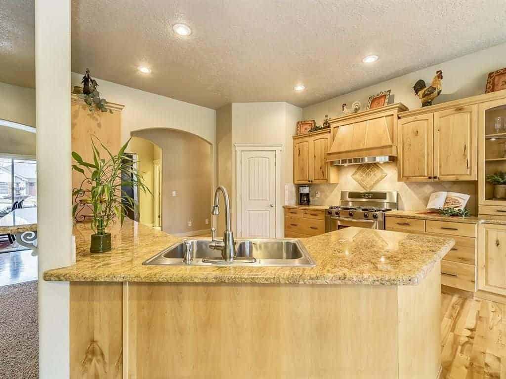 Light wood cabinetry matches the hardwood flooring and peninsula that's topped with a granite counter and undermount sink. It is illuminated by recessed lights mounted on the regular white ceiling.