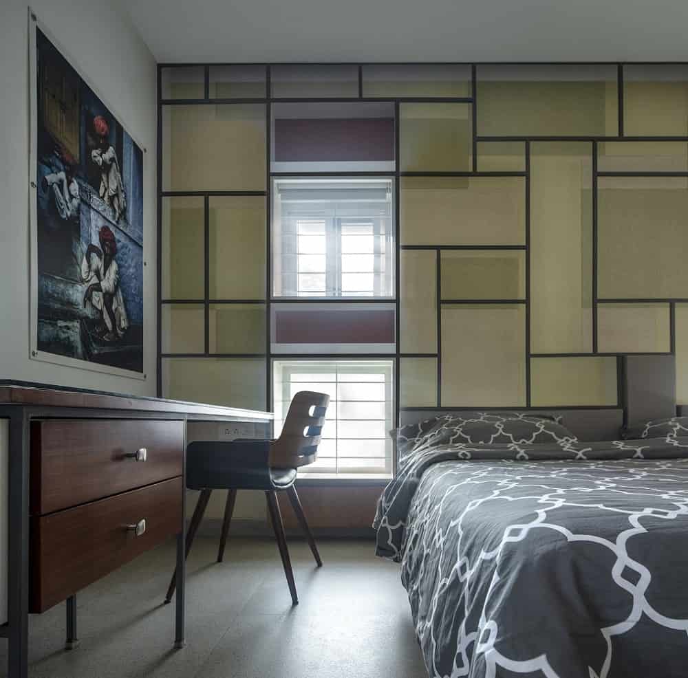 This is a close look at the bedroom that has a large platform bed with dark patterned sheets adorned by the patterned beige wall behind the headboard and the wall-mounted artwork above the study area with a wooden desk.