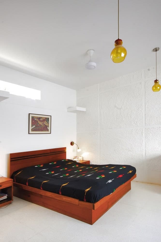 This is the simple bedroom with white floor, walls and ceiling. These make the brown wooden platform bed stand out with its dark patterned sheets along with its matching bedside tables.